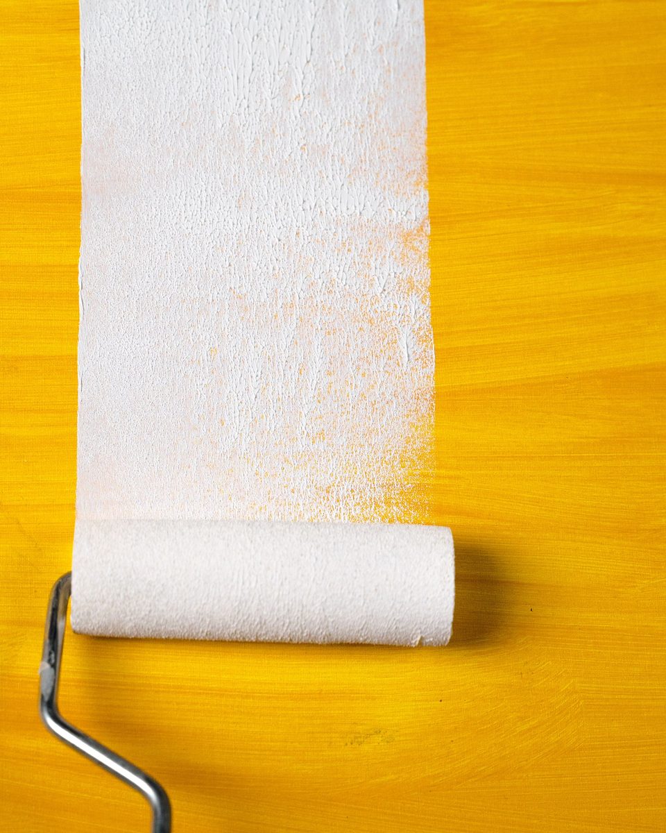 Representative photo: a paint roller laying a fresh white stripe over a yellow surface